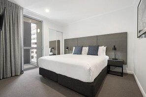 A hotel room with a large bed, a bedside table, a nightstand, and a view of the outside through a sliding door. - Oaks Toowoomba Hotel (Toowoomba)