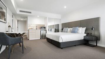 A modern hotel room with a large bed, bedside tables, a desk, and a kitchenette.