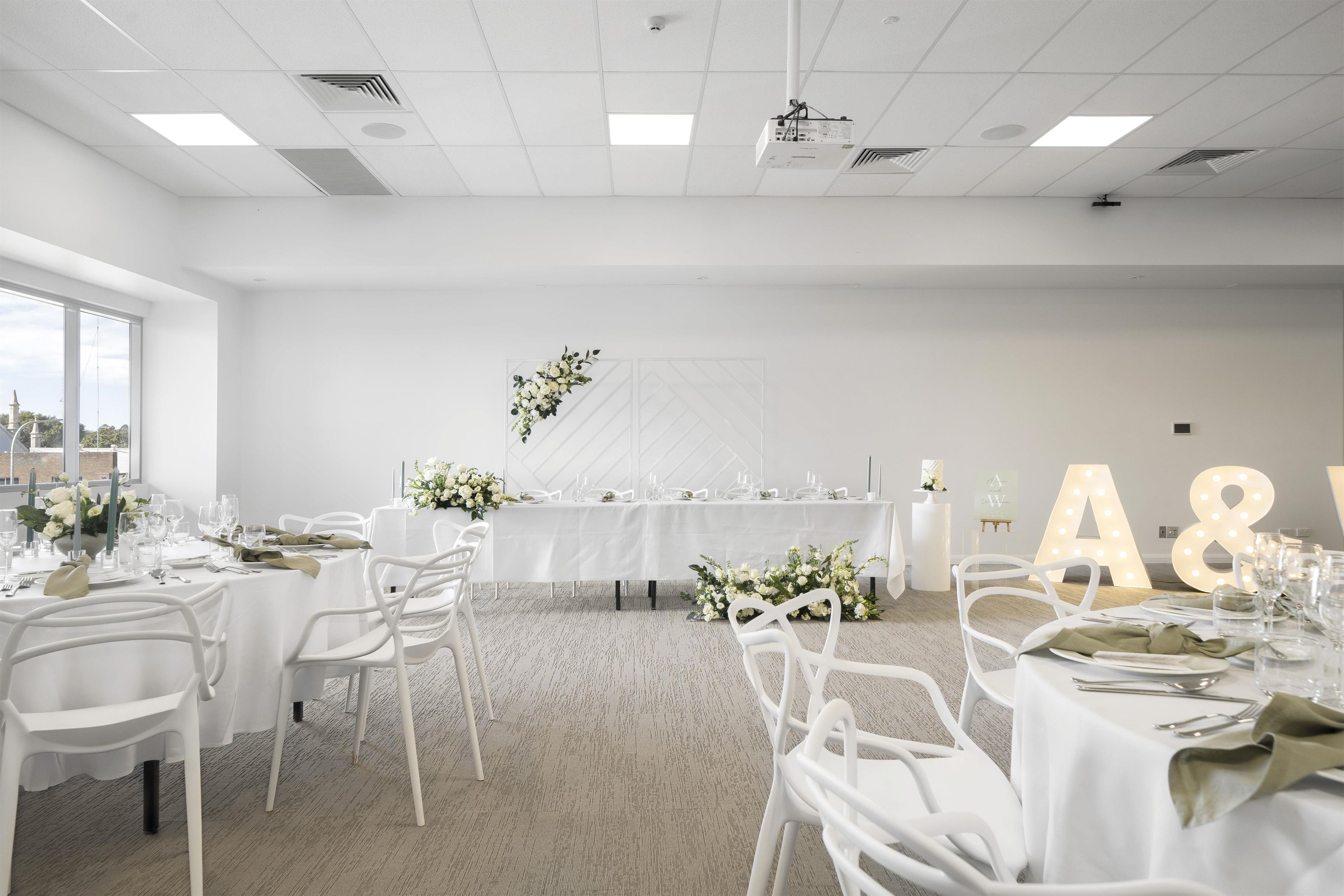 Amplia habitación con varias mesas dispuestas para comer, con manteles blancos y sillas.