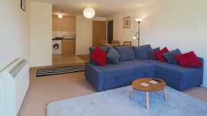 A modern living room with a blue sectional sofa, a small wooden coffee table, and a white shaggy rug. - Bingley Court (Canterbury)