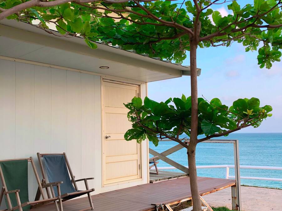 Eine Strandhütte mit Holzterrasse, zwei Liegestühlen und Blick auf den Ozean.