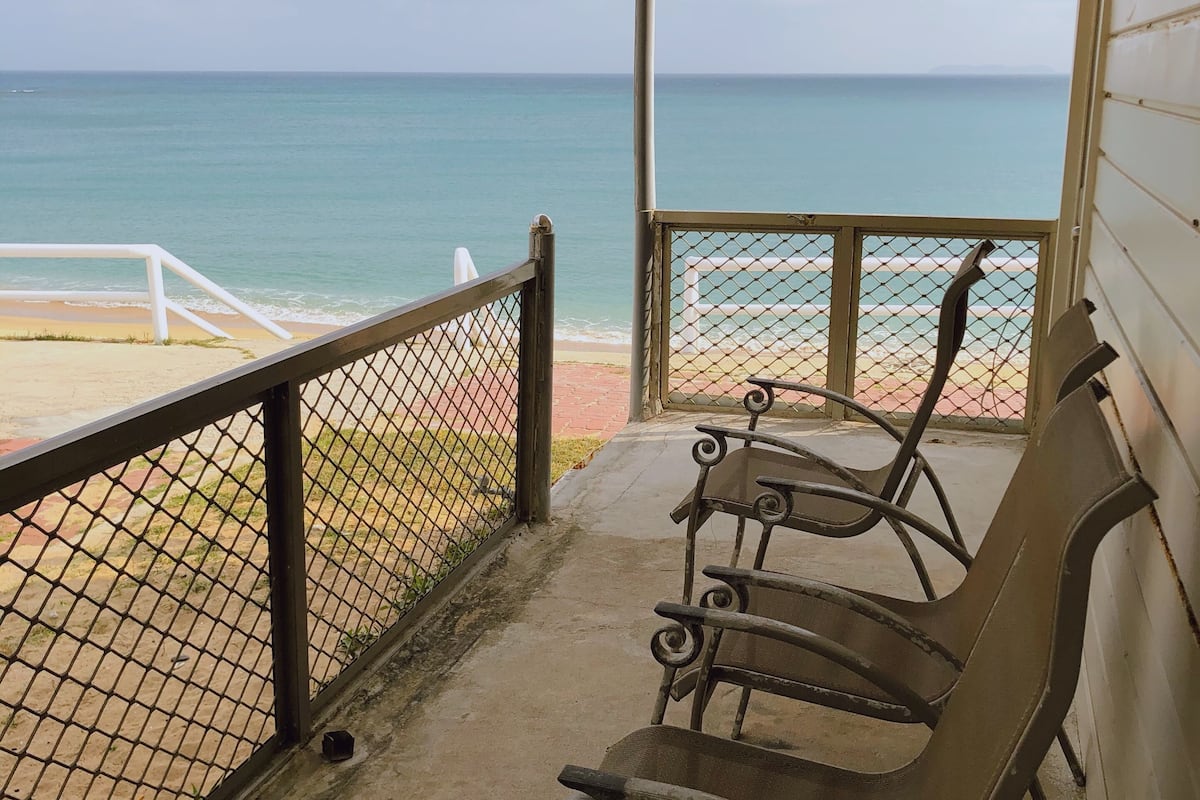 A covered outdoor seating area with metal chairs and a view of the beach and ocean.