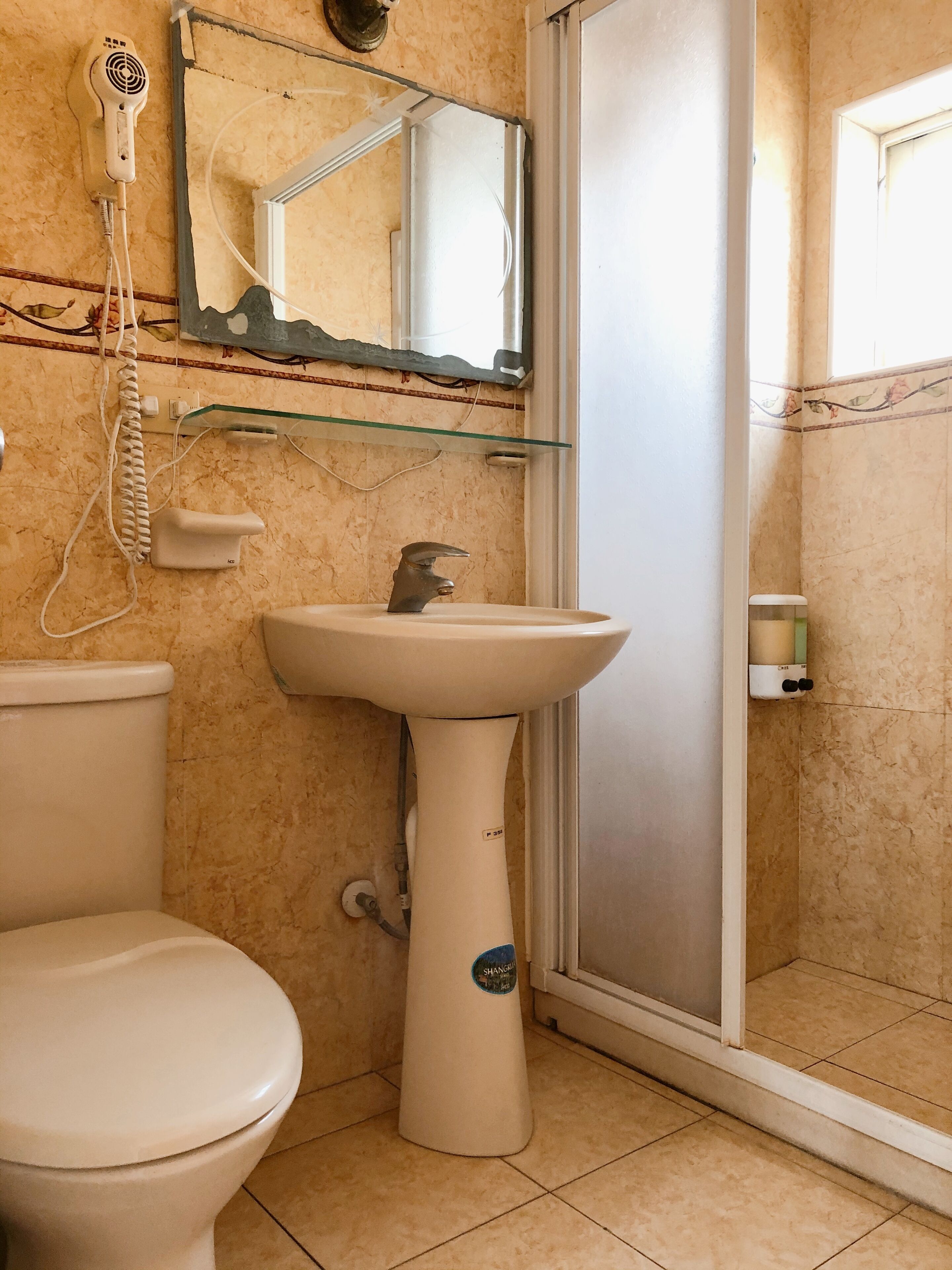Baño con inodoro, lavamanos pedestal y cabina de ducha de cristal.