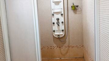 Um espaço de chuveiro pequeno revestido com azulejos, com porta branca, chuveiro fixo e mangueira.