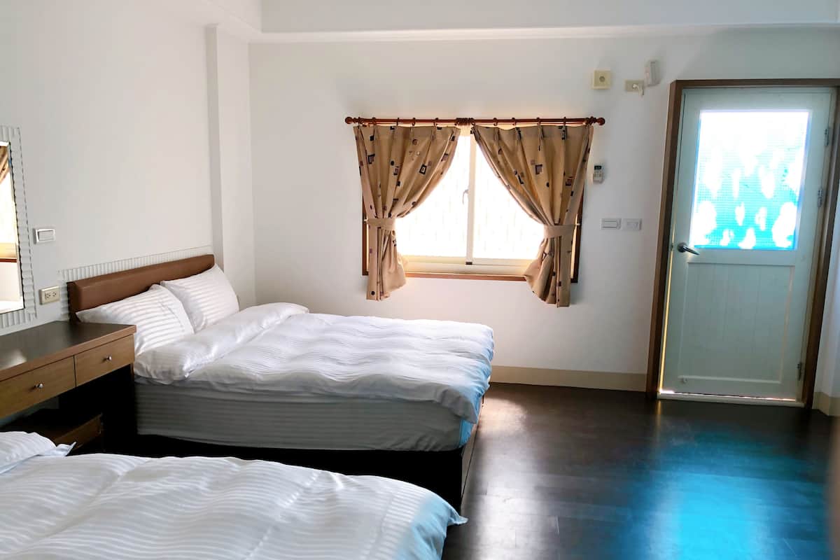 A hotel room with two beds, a wooden dresser, a window with curtains, and a door.