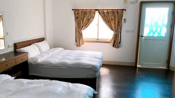 A hotel room with two beds, a wooden dresser, a window with curtains, and a door.