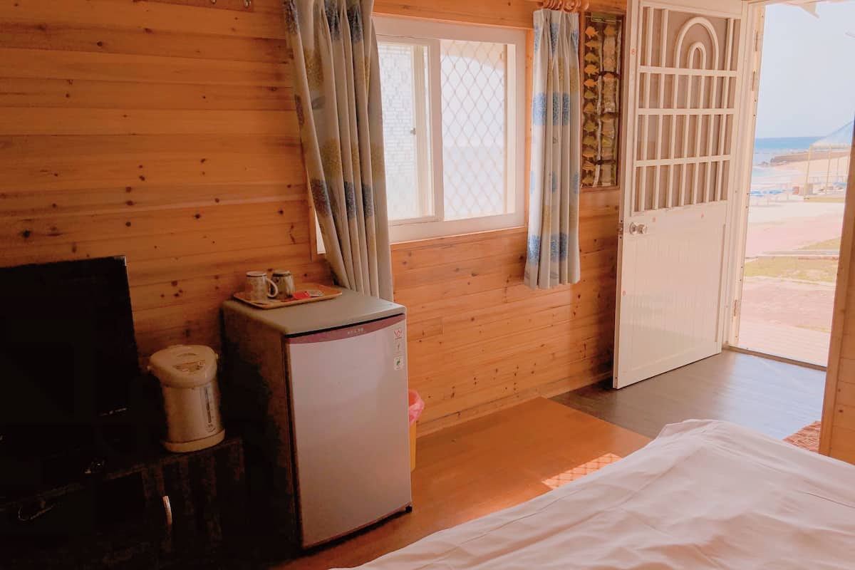 A wooden room with a bed, a small refrigerator, a television, and a window with curtains.
