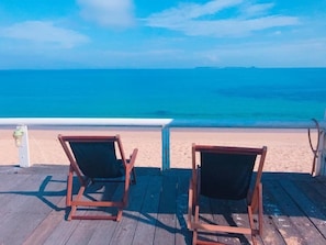 Two wooden lounge chairs on a wooden deck overlooking a beach with clear blue water and a distant shoreline. - Zhixianwu Homestay (Wangan)