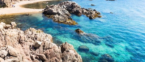 A coastal landscape with clear blue waters, rocky terrain, and a sandy beach.