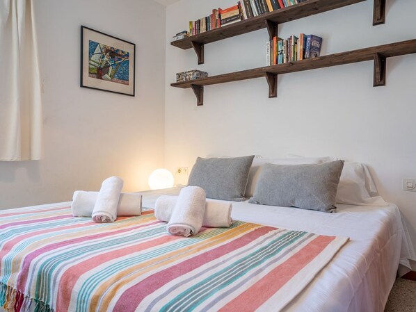 Un lit bien fait, avec une literie à rayures, une lampe de chevet et une bibliothèque remplie de livres.
