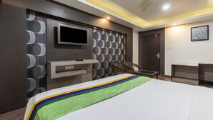 Een moderne hotelkamer met een groot bed, een flatscreen televisie bevestigd aan een muur met ronde patronen, een plafondventilator en een deur met uitzicht op zee.
