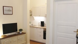 A compact living space with a TV on a wooden cabinet, a small potted plant, and a kitchen area with white cabinets and a coffee maker. - Bircks Apartments Bremen (Bremen)