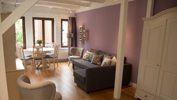 A modern living room with a grey sofa, a dining table with chairs, and a staircase leading to another level. - Bircks Apartments Bremen (Bremen)