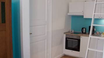 Una cocina compacta con armarios blancos, piso de madera y una pared de acento color aguamarina.
