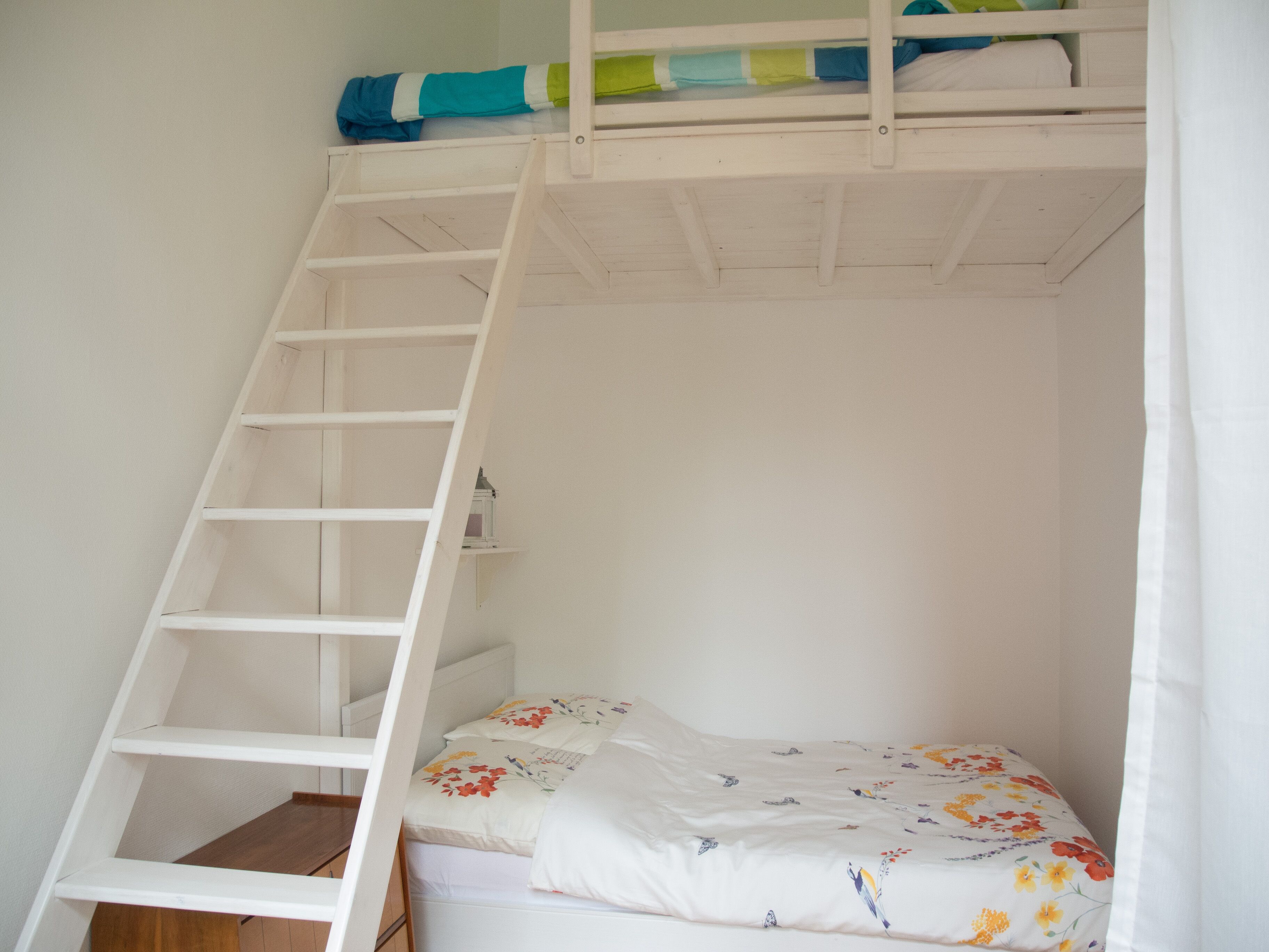 A bunk bed with a ladder, a small shelf, and a floral-patterned bedspread.