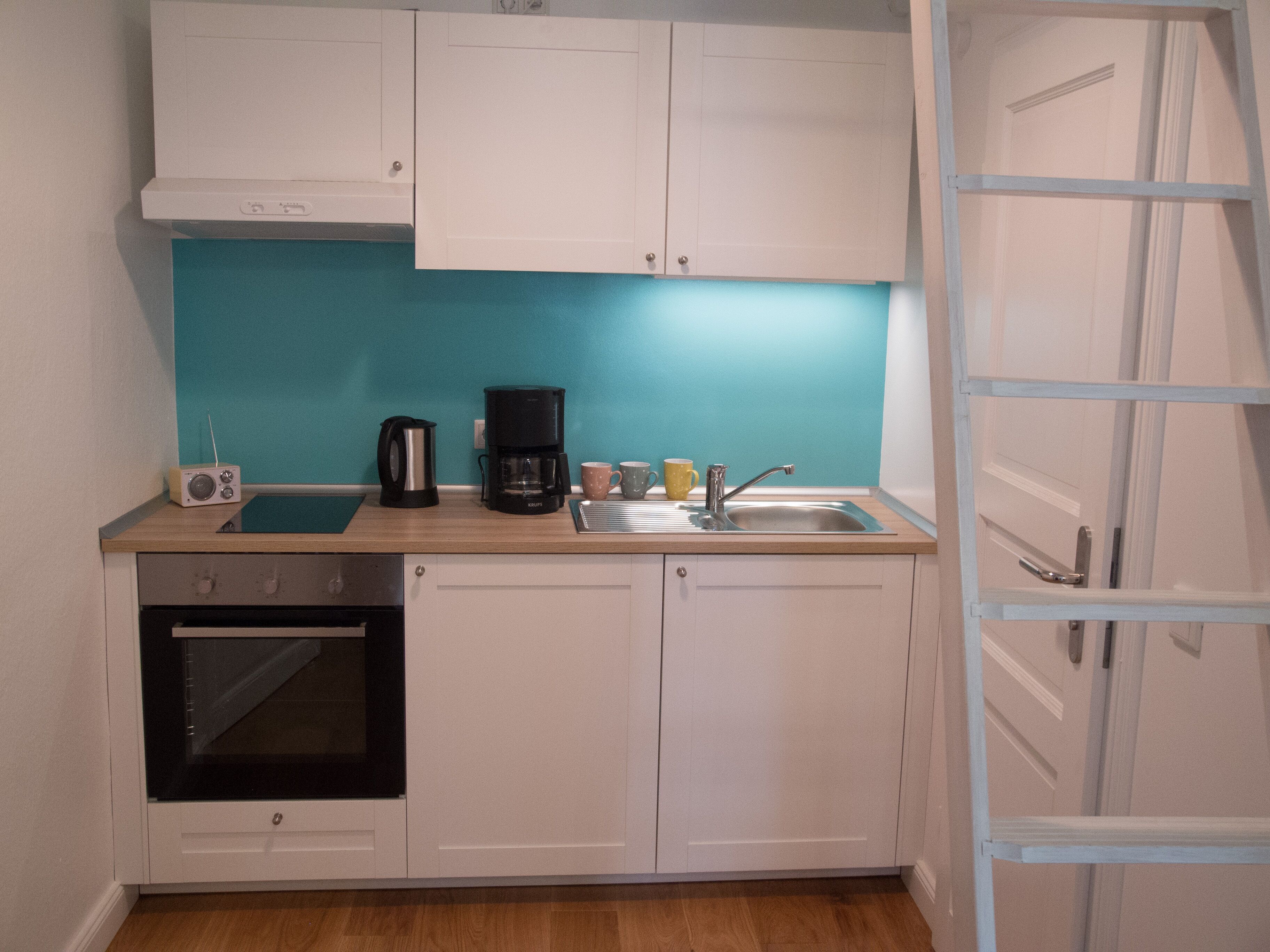 Una cucina compatta con mobili bianchi, una macchina da caffè nera, un bollitore e una piccola radio.