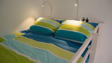 Una cama con estructura blanca, ropa de cama a rayas en azul, verde y amarillo, y dos lámparas de noche.