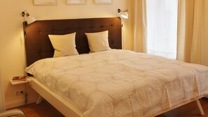 A neatly made bed with a headboard, a bedside lamp, and a nightstand with a book and a phone. - Bircks Apartments Bremen (Bremen)