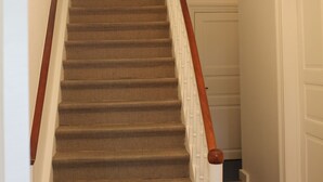 A staircase with a patterned carpet, a wooden handrail, and a chandelier. - Bircks Apartments Bremen (Bremen)