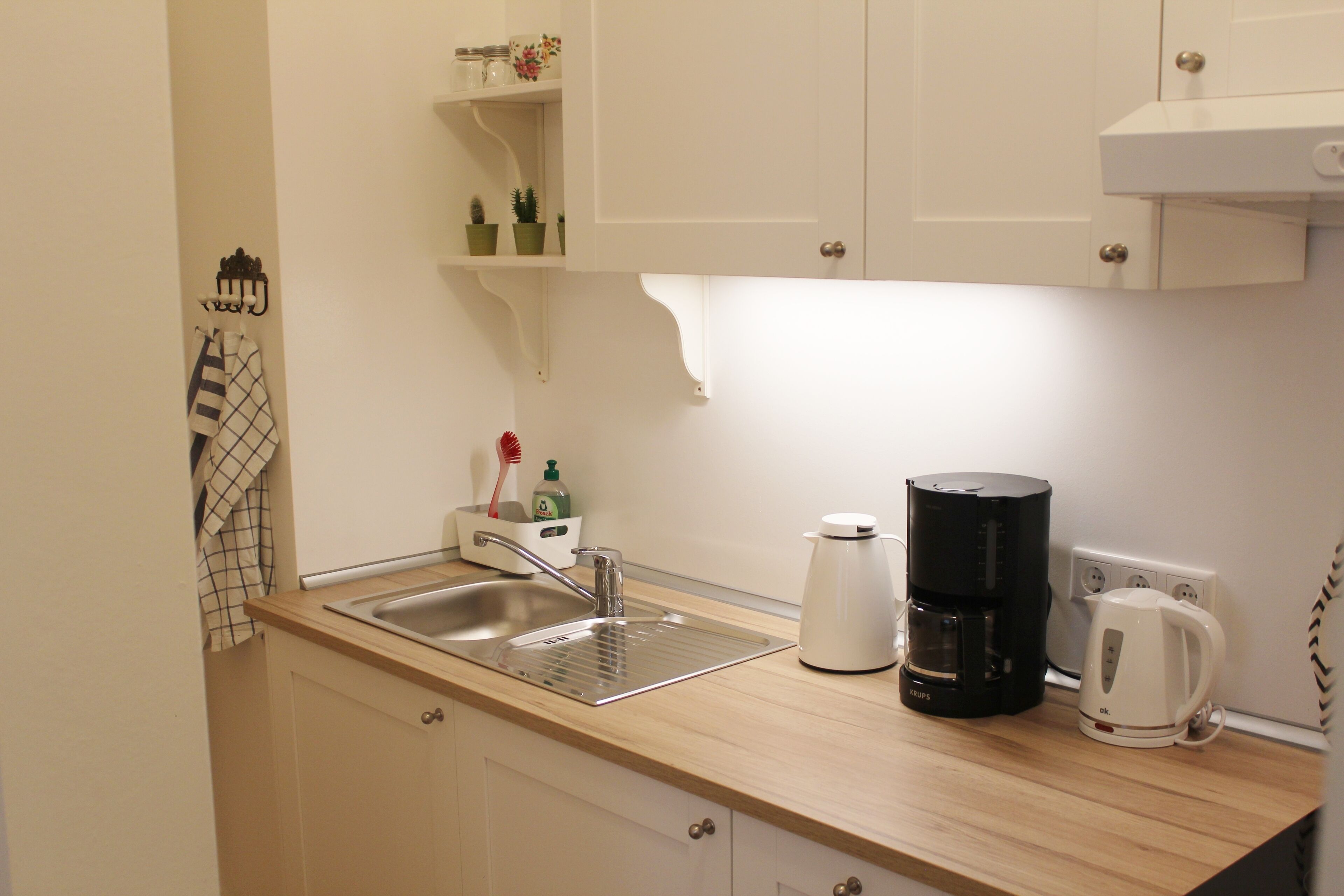A kitchen with a sink, a coffee maker, and a kettle. There are cabinets and a countertop.