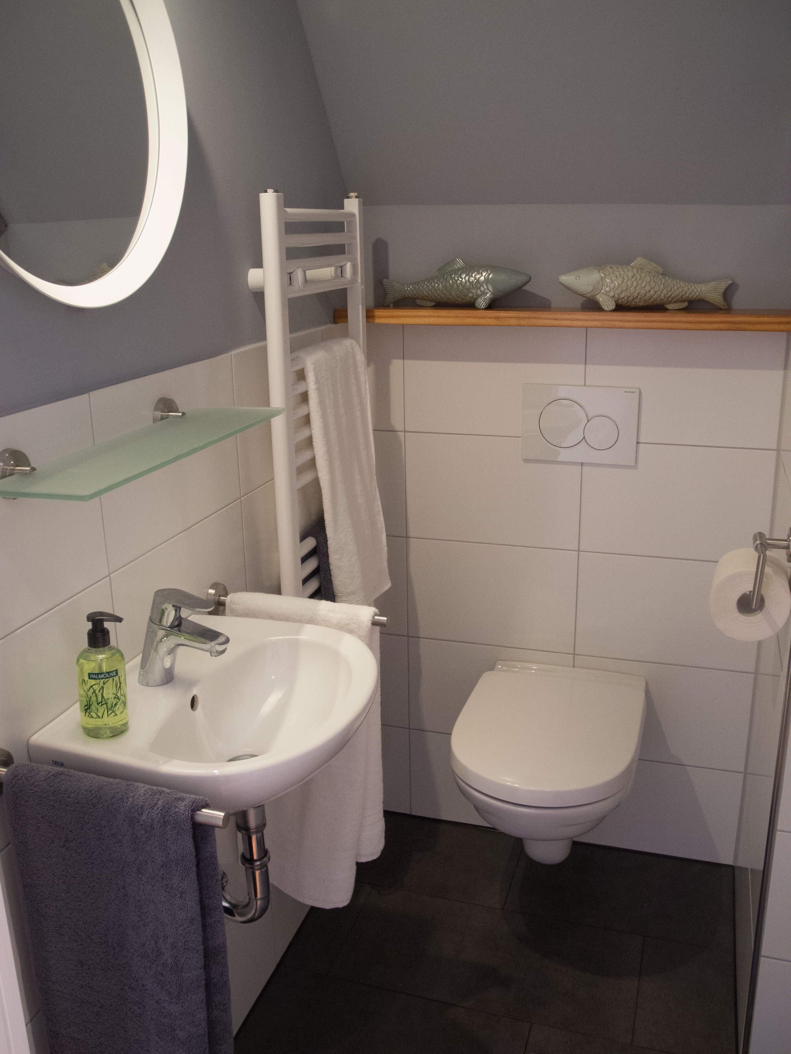 Une salle de bain avec un lavabo blanc, un bidet, un porte-serviettes et une étagère décorée de poissons.