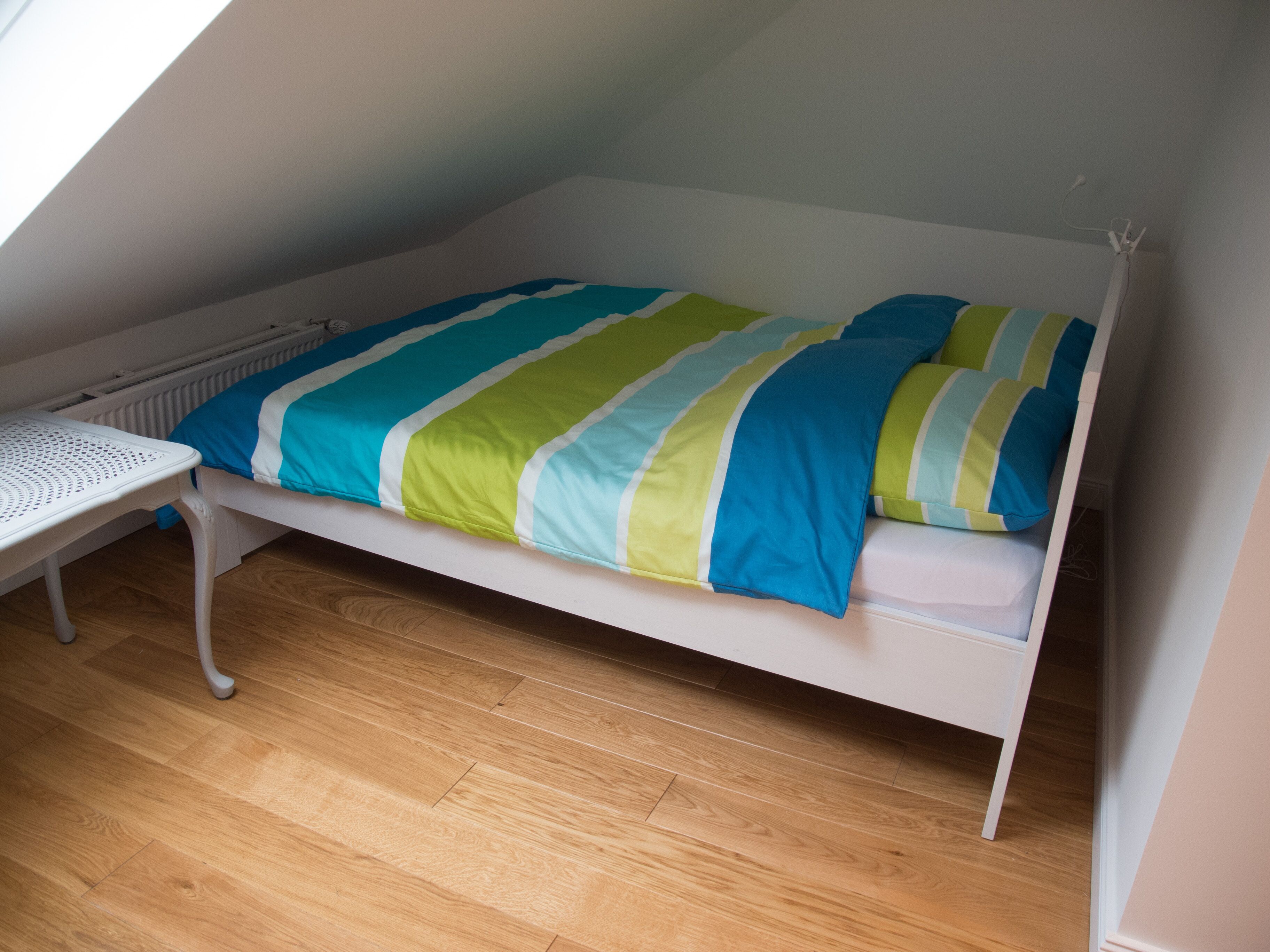 A single bed with a striped bedspread in a room with wooden flooring and a white radiator.