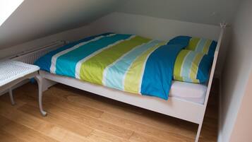A single bed with a striped bedspread in a room with wooden flooring and a white radiator.