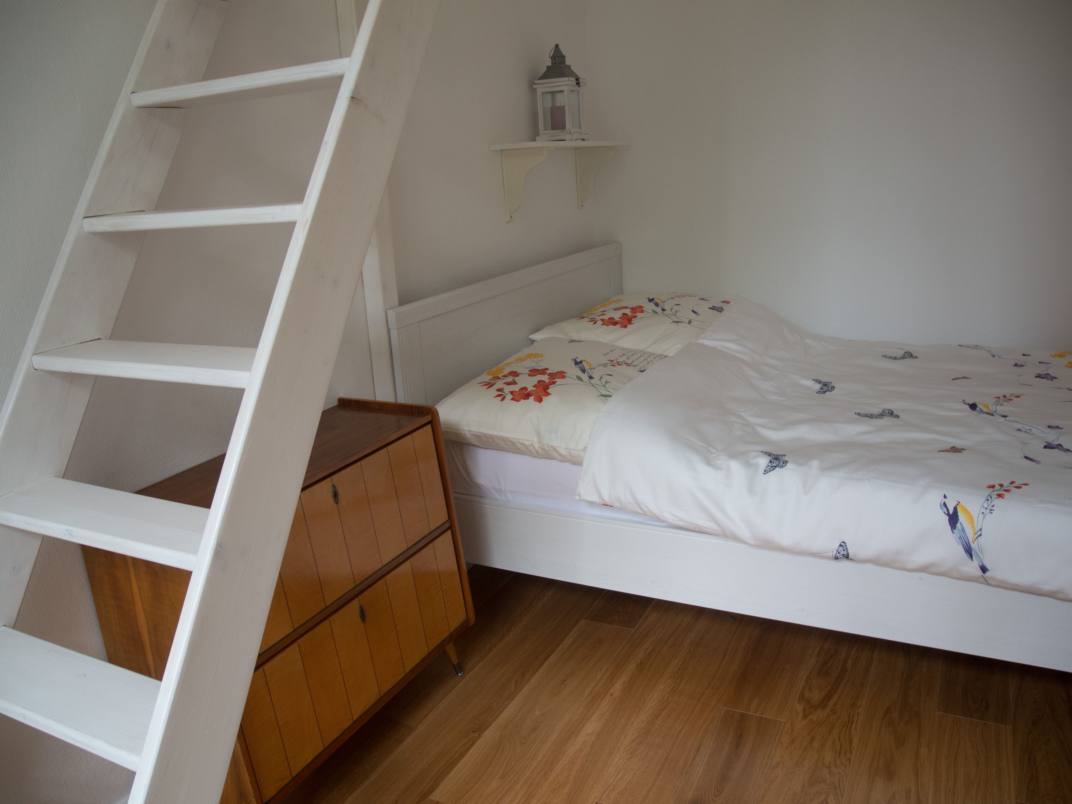 Een slaapkamer met een houten bed, een witte kapstok en een houten trap.