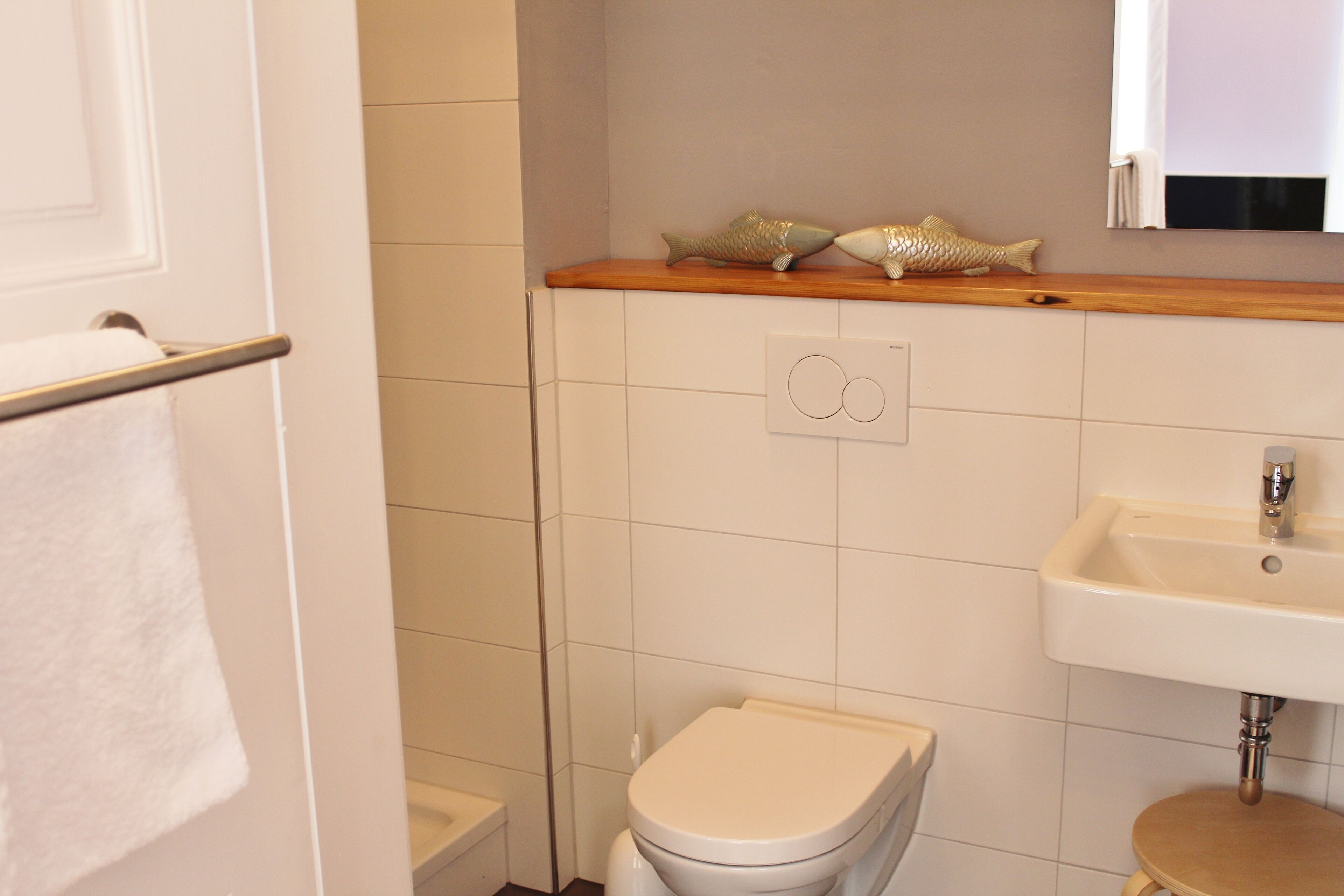 A bathroom with a toilet, sink, and decorative fish on the shelf.