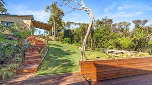 Une maison moderne dotée d’une terrasse en bois, d’un escalier en colimaçon et de diverses plantes tropicales.
