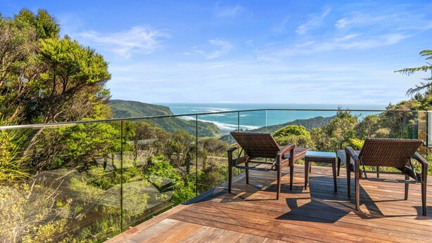 Une terrasse en bois avec des fauteuils en osier donnant sur un paysage côtier.