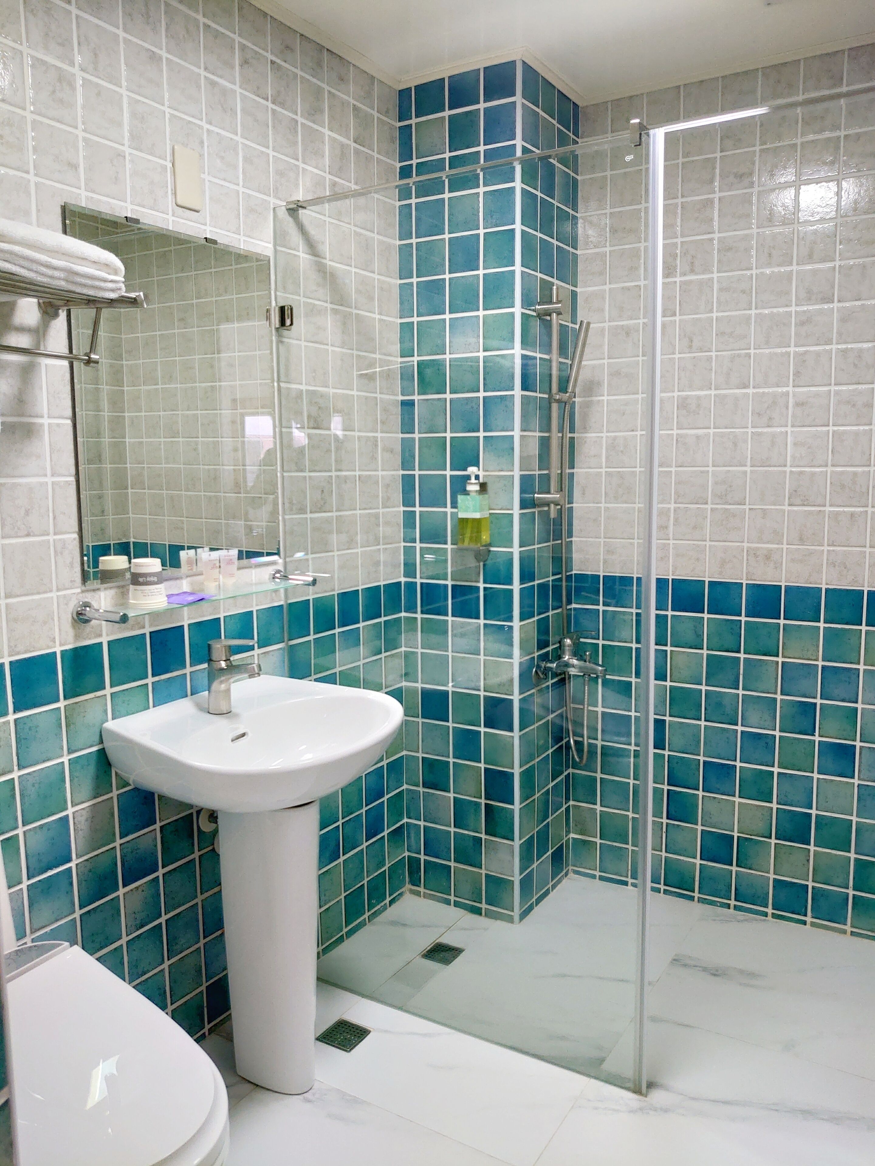 Un baño con lavamanos blanco, cabina de ducha con mampara de vidrio y paredes con azulejos azules.