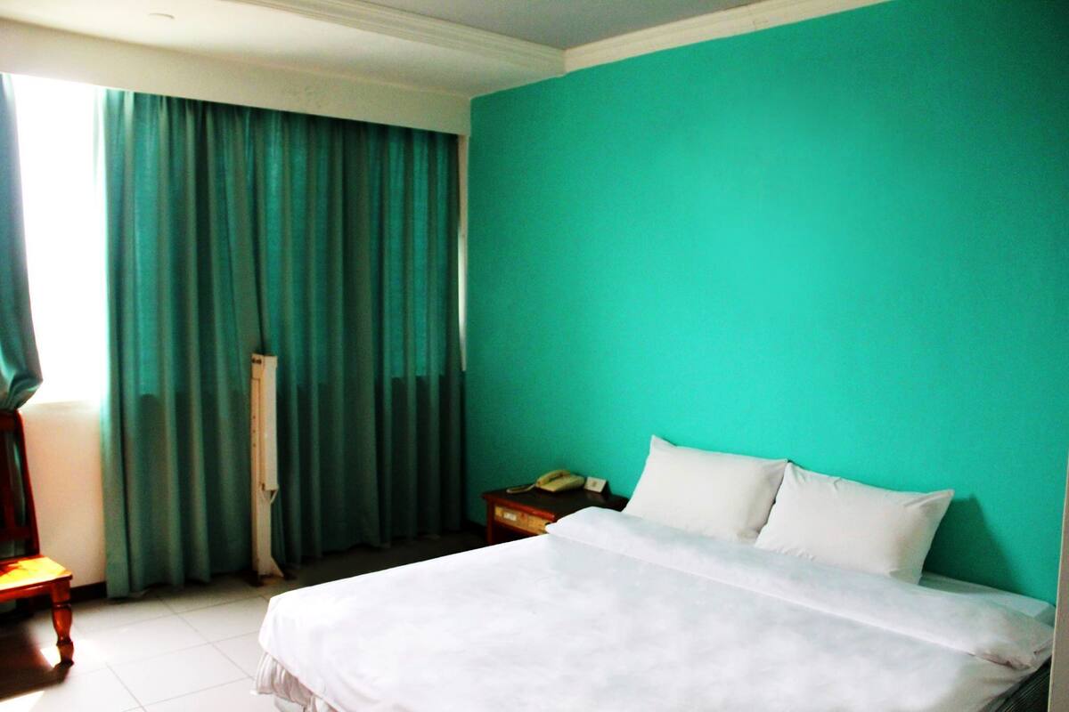A hotel room with a bed, a nightstand, a telephone, and a window with curtains.