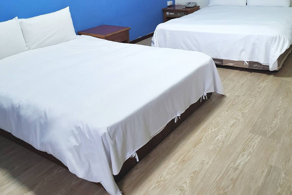 A hotel room with two beds, a wooden floor, and a blue accent wall.