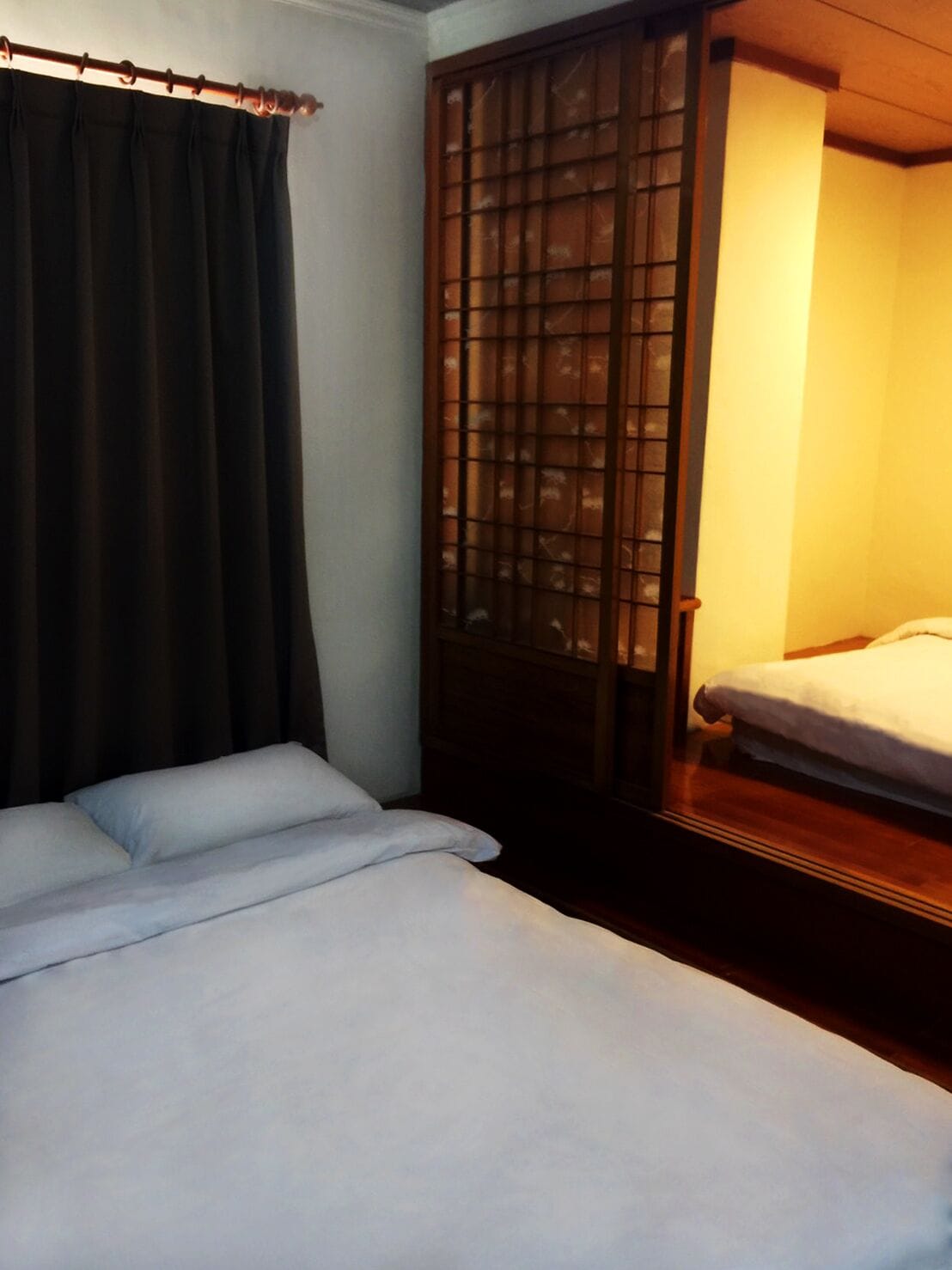 A single bed with white bedding, a dark curtain, and a wooden wardrobe with a glass door.
