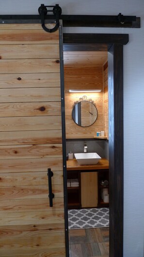 A wooden sliding door leading to a bathroom with a mirror, sink, and towel storage. - Ryder's House (Hakuba)