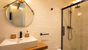 Ein Badezimmer mit weißem Waschbecken, rundem Spiegel und einer Duschkabine aus Glas.