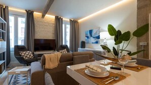 Ein modernes Wohnzimmer mit einer Couch, einem Sessel und einem Essbereich mit Tisch für zwei Personen.