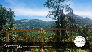 A view from a wooden balcony with a wooden railing, overlooking a lush landscape with a prominent tree and hills in the distance. - Homely Stay Balana Kapolla (Mawanella)