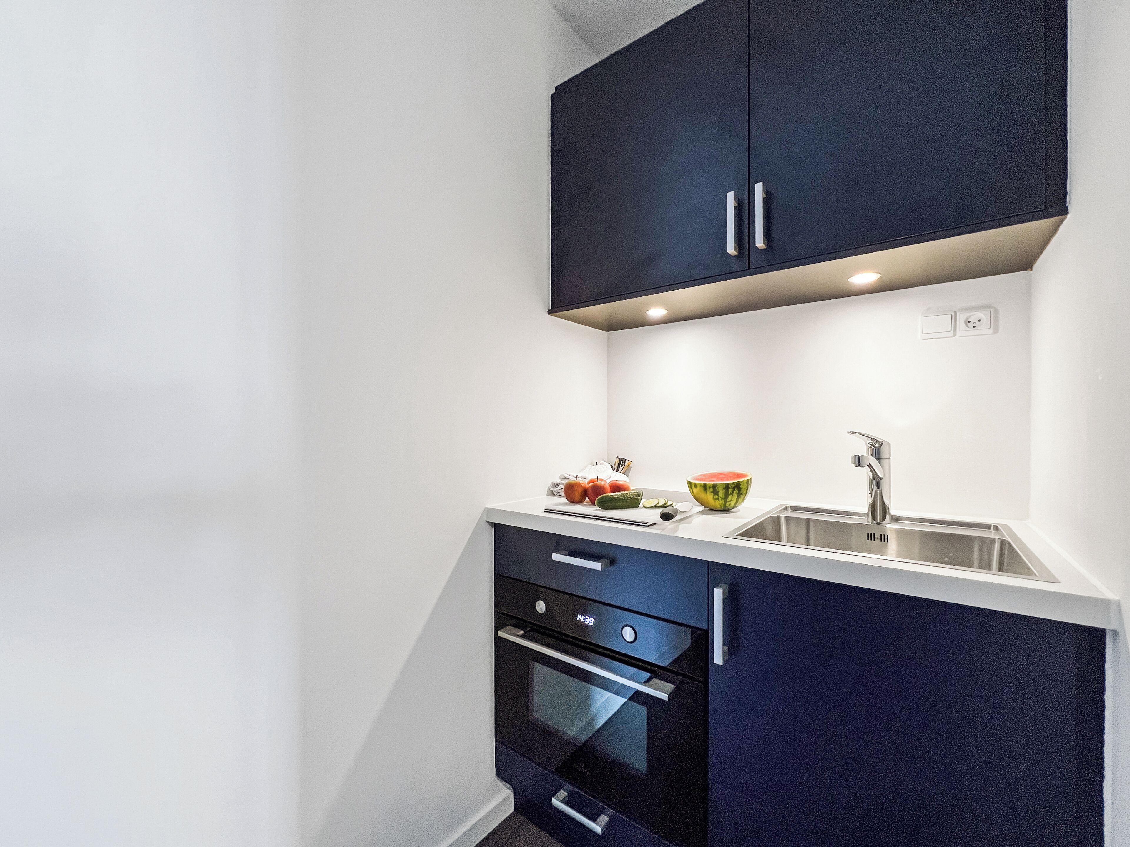 A compact kitchen with dark cabinetry, a white countertop, a sink, and a built-in oven.