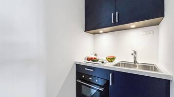 A compact kitchen with dark cabinetry, a white countertop, a sink, and a built-in oven.