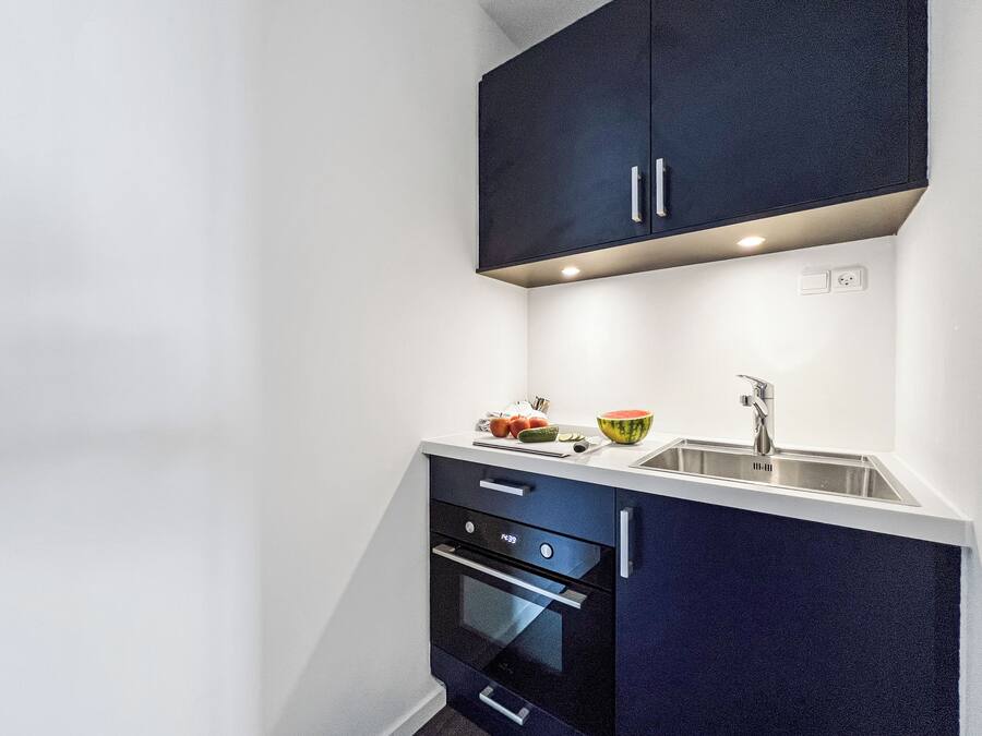 A compact kitchen with dark cabinetry, a white countertop, a sink, and a built-in oven.