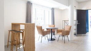 A modern hotel room with a dining area featuring a round table and four chairs, a wooden partition, and a large window with curtains. - Hotel Nordbo (Nuuk)