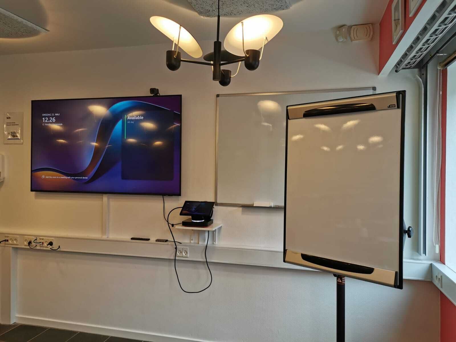 A conference room with a large flat-screen TV displaying a presentation, a whiteboard, and a projector.