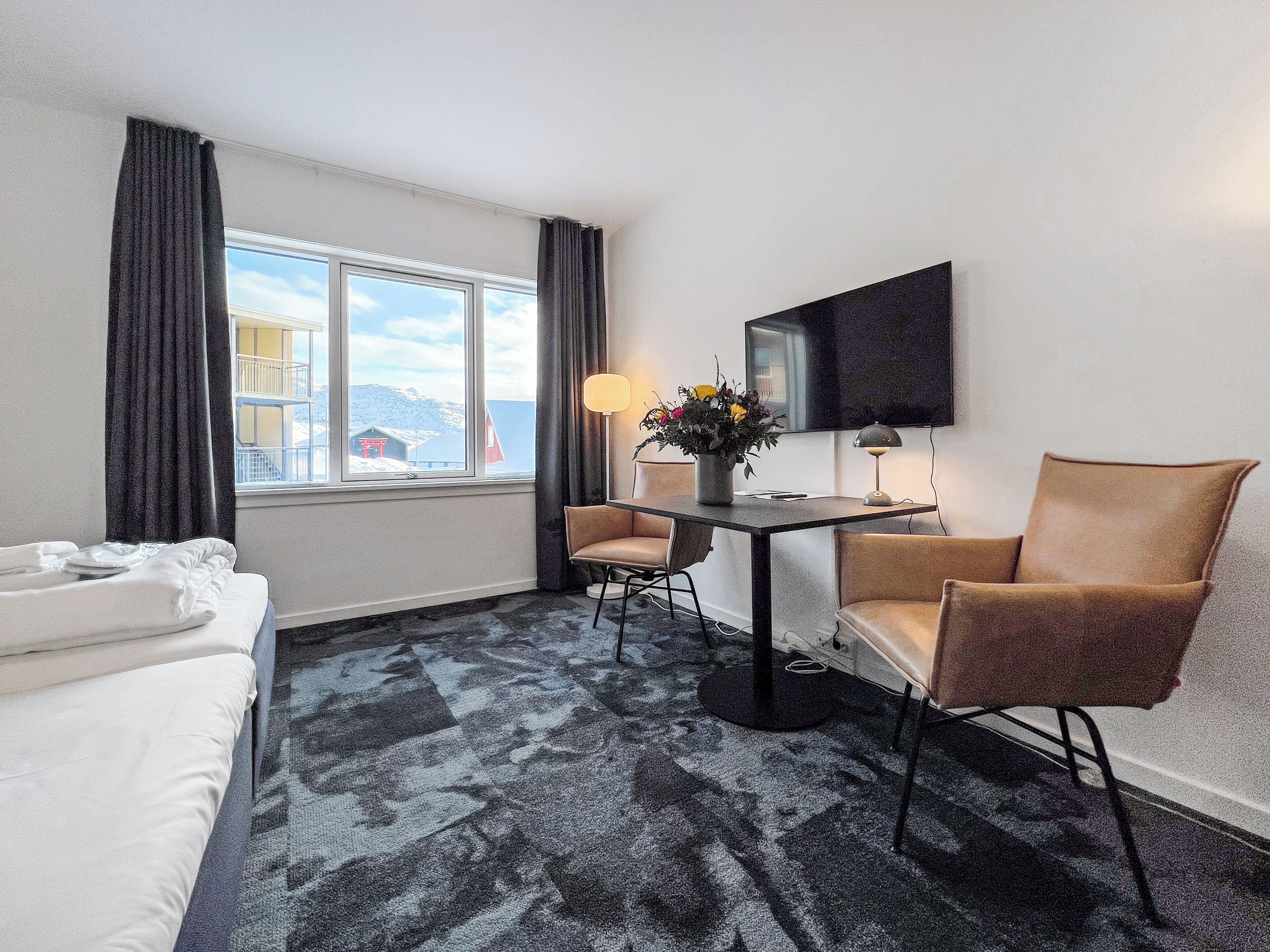 Ein Hotelzimmer mit Bett, Schreibtisch mit Stuhl, Fernseher und Blick auf eine verschneite Landschaft.