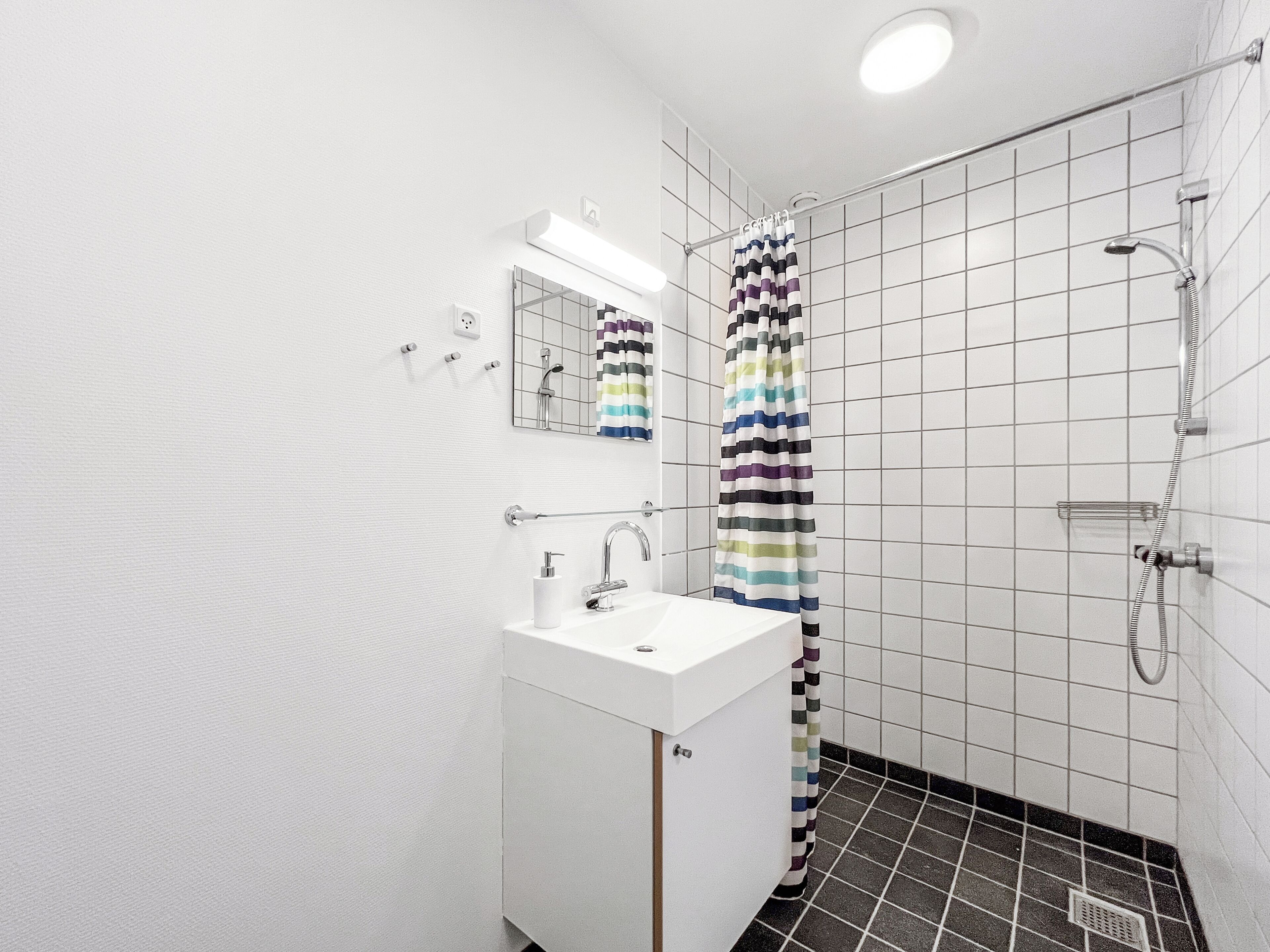 Un baño moderno con un lavabo blanco, espejo y ducha.