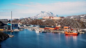 A coastal town with buildings, boats, and a mountain in the background. - Hotel Nordbo (Nuuk)