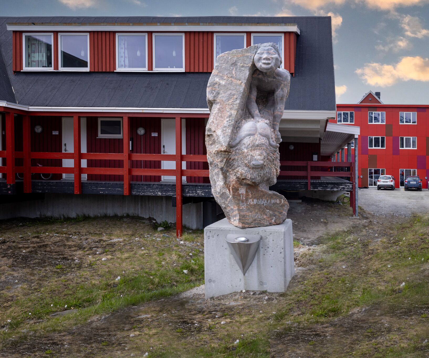 A stone sculpture in front of a building with red and white exterior walls and a grey roof.