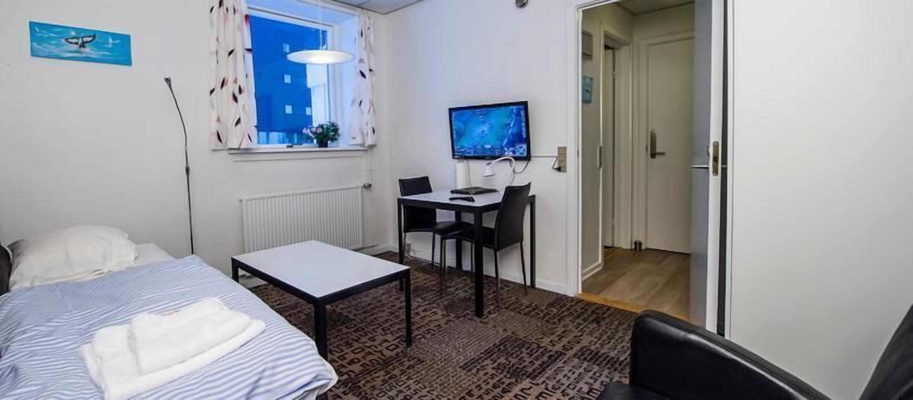 Un dormitorio con cama, escritorio, silla, televisor y ventana con cortinas.
