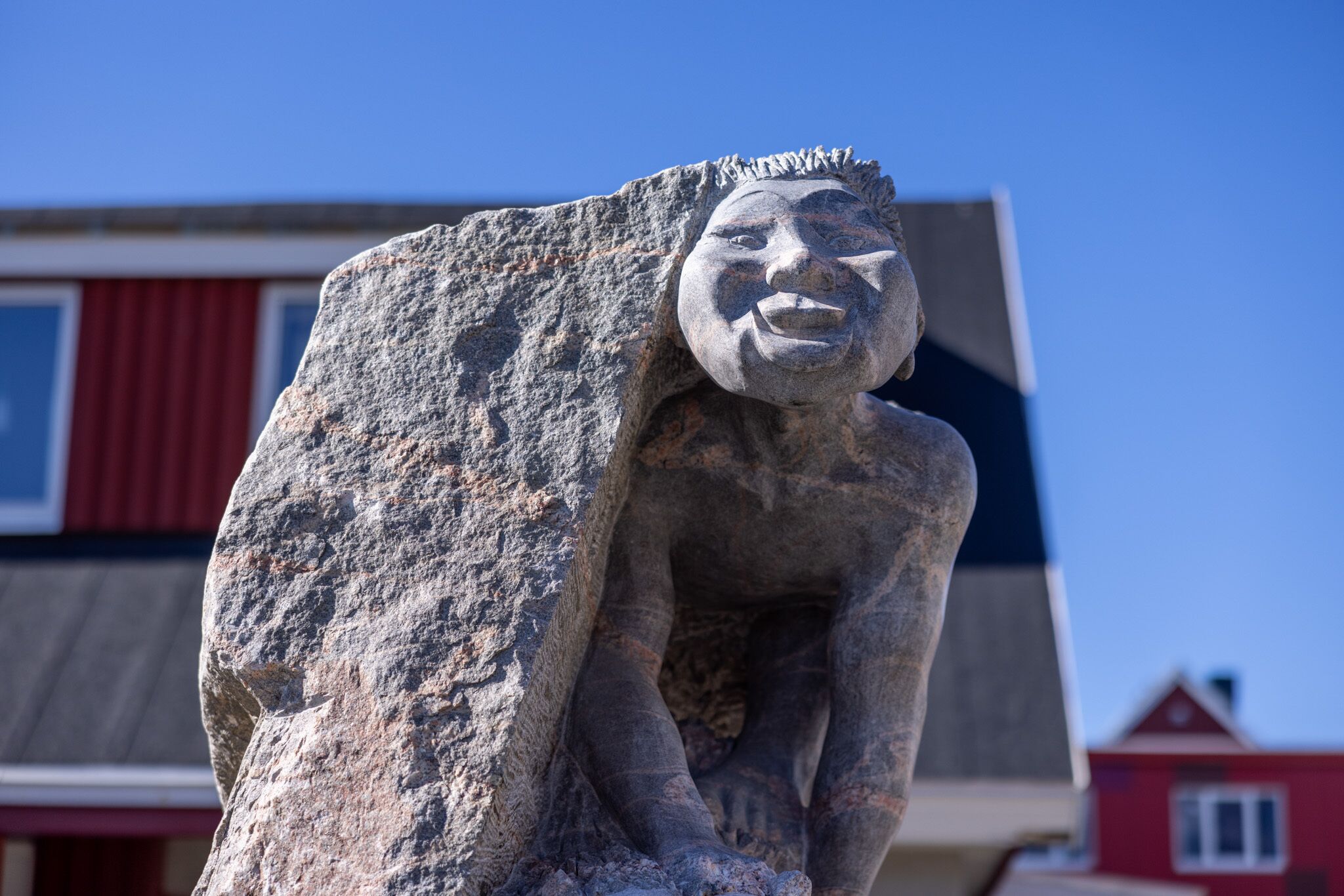 A stone sculpture of a figure with a large rock as a backdrop.